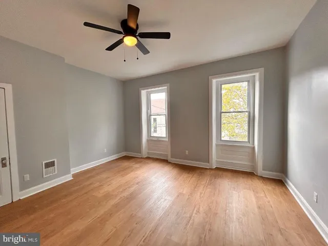an empty room with wooden floor chandelier fan and windows