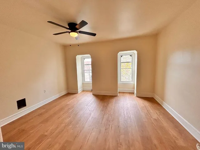 an empty room with wooden floor ceiling fan and windows