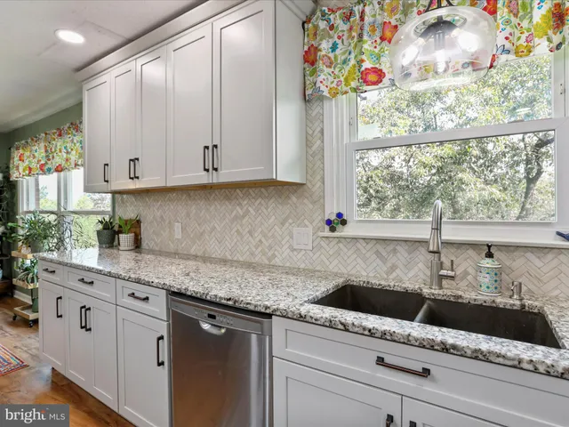 a kitchen with stainless steel appliances granite countertop a sink a window and a white cabinets