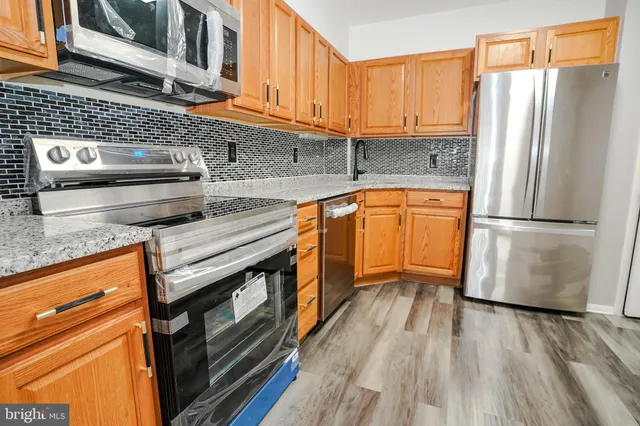 a kitchen with stainless steel appliances granite countertop a refrigerator a sink dishwasher a stove and white countertops with wooden floor