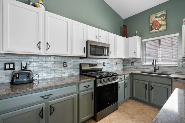 a kitchen with stainless steel appliances granite countertop grey cabinets a stove a sink and a microwave
