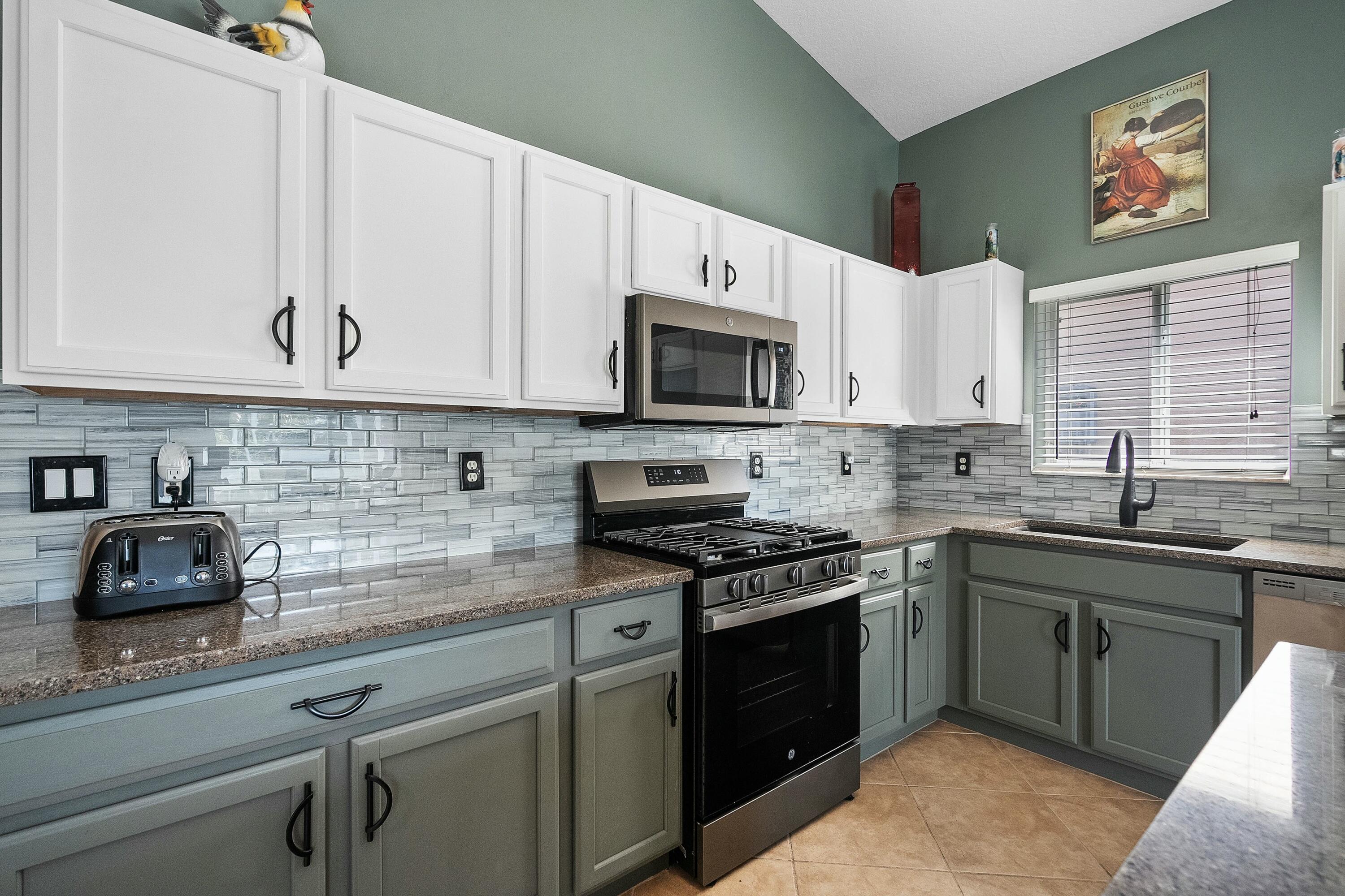 2480 Southeast Springtree Place Stuart, FL 34997 - Photo 10 of 39 a kitchen with stainless steel appliances granite countertop grey cabinets a stove a sink and a microwave
