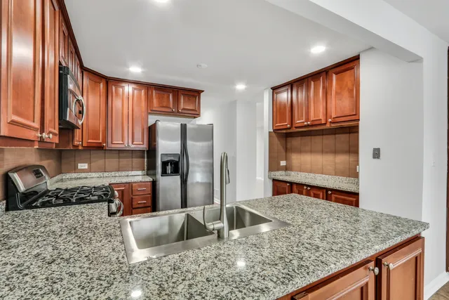a kitchen with stainless steel appliances granite countertop a refrigerator a stove and a sink with wooden floor
