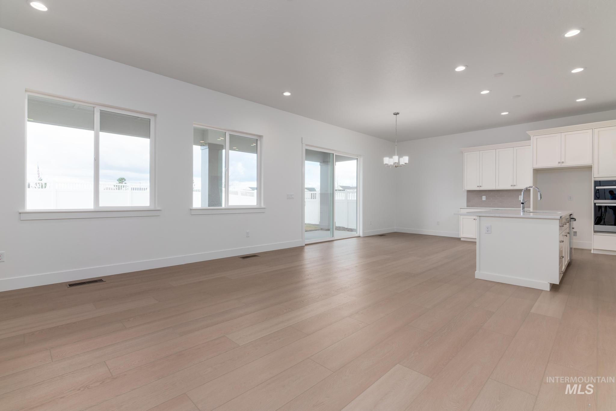 8501 South Country Wind Avenue Meridian, ID 83642 - Photo 37 of 38 Kitchen featuring suspended lighting, white cabinetry, a center island with sink, light wood finished floors, and open floor plan