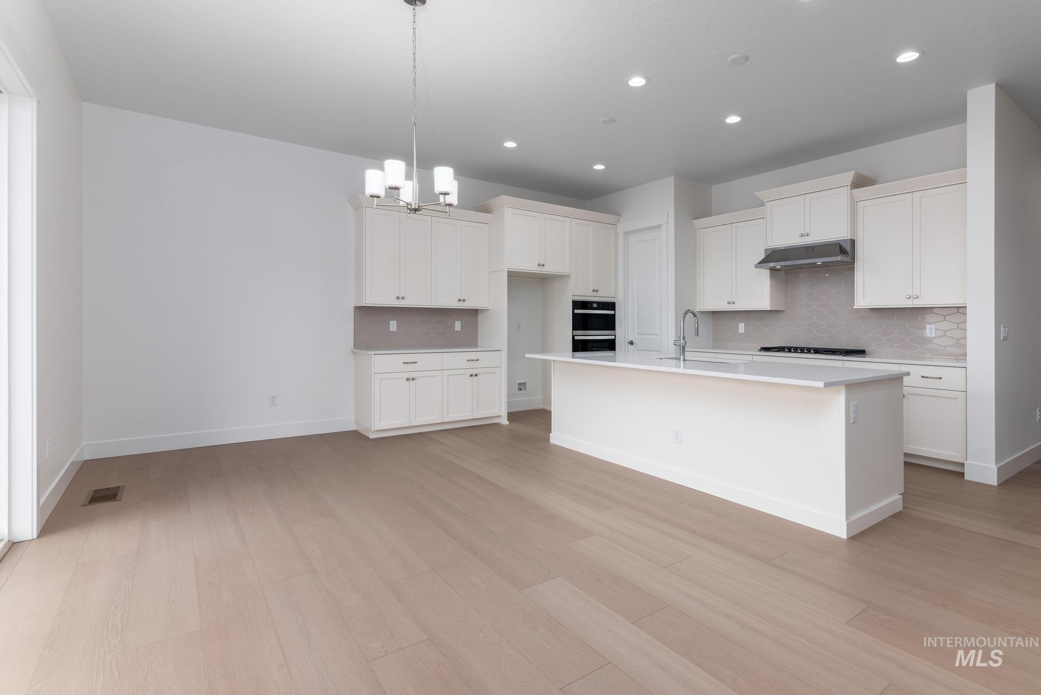 8501 South Country Wind Avenue Meridian, ID 83642 - Photo 6 of 38 Kitchen with white cabinets, a chandelier, tasteful backsplash, a kitchen island with sink, and light wood-style floors