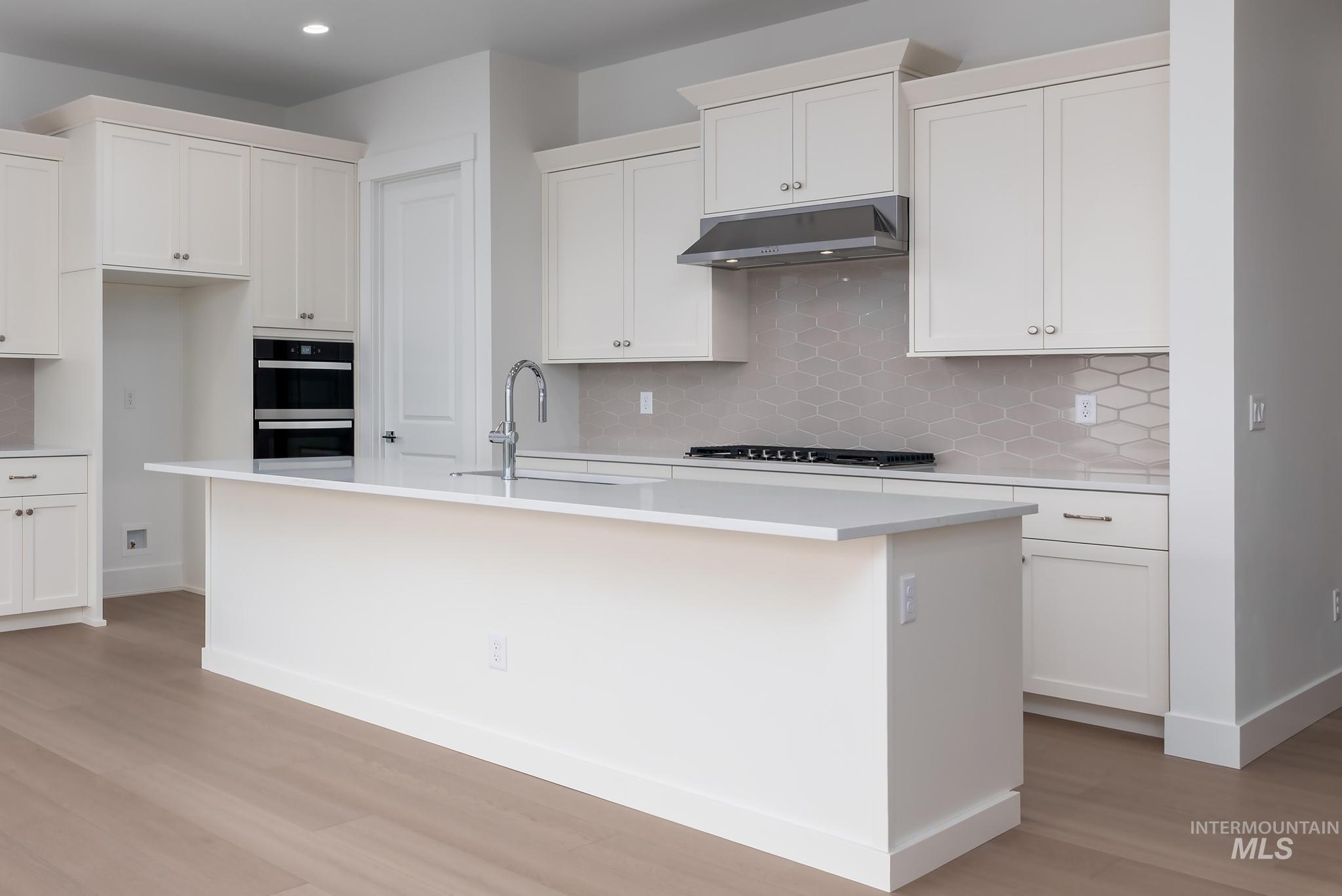 8501 South Country Wind Avenue Meridian, ID 83642 - Photo 7 of 38 Kitchen featuring a center island with sink, white cabinets, light wood-style floors, multiple ovens, and decorative backsplash