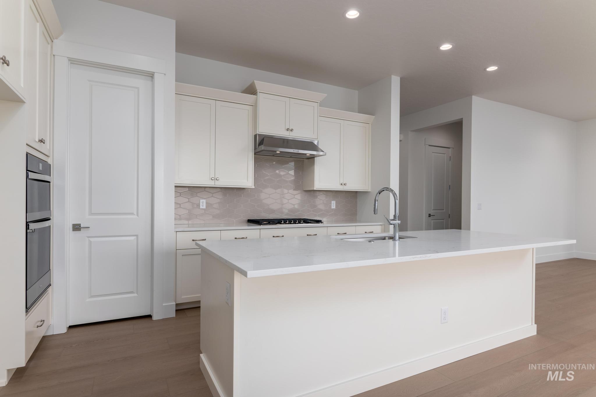8501 South Country Wind Avenue Meridian, ID 83642 - Photo 8 of 38 Kitchen featuring white cabinetry, an island with sink, light stone countertops, light wood-style floors, and recessed lighting