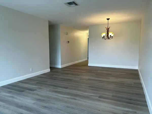 an empty room with wooden floor chandelier and windows