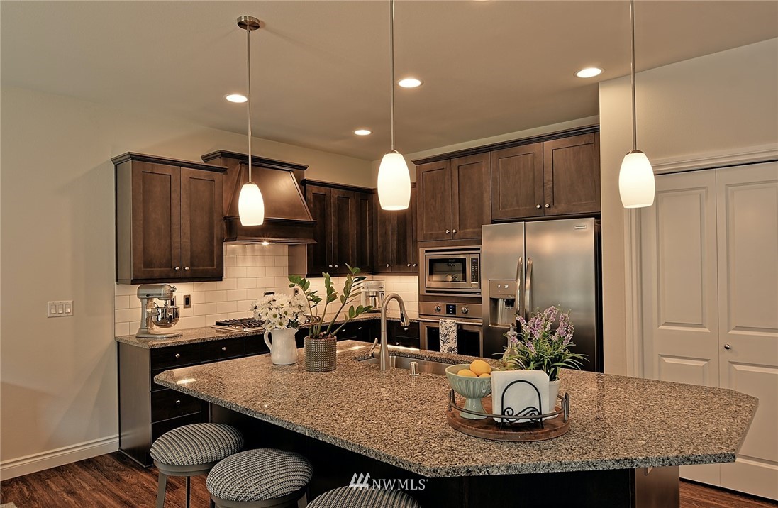20322 85th Place Northeast Bothell, WA 98011 - Photo 2 of 24 a kitchen with kitchen island granite countertop a sink a refrigerator and chairs with wooden floor