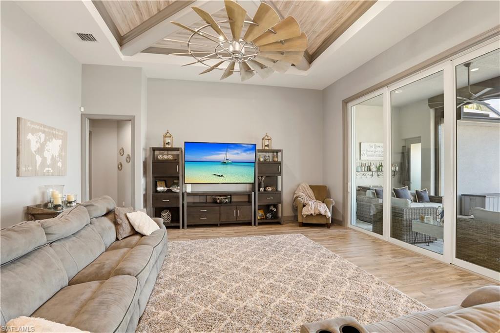 1616 Old Burnt Store Road North Cape Coral, FL 33993 - Photo 11 of 50 Sit back and relax while you watch TV and the outdoor activity at the same time. Living room featuring a ceiling fan, wood finished floors, and a tray ceiling.