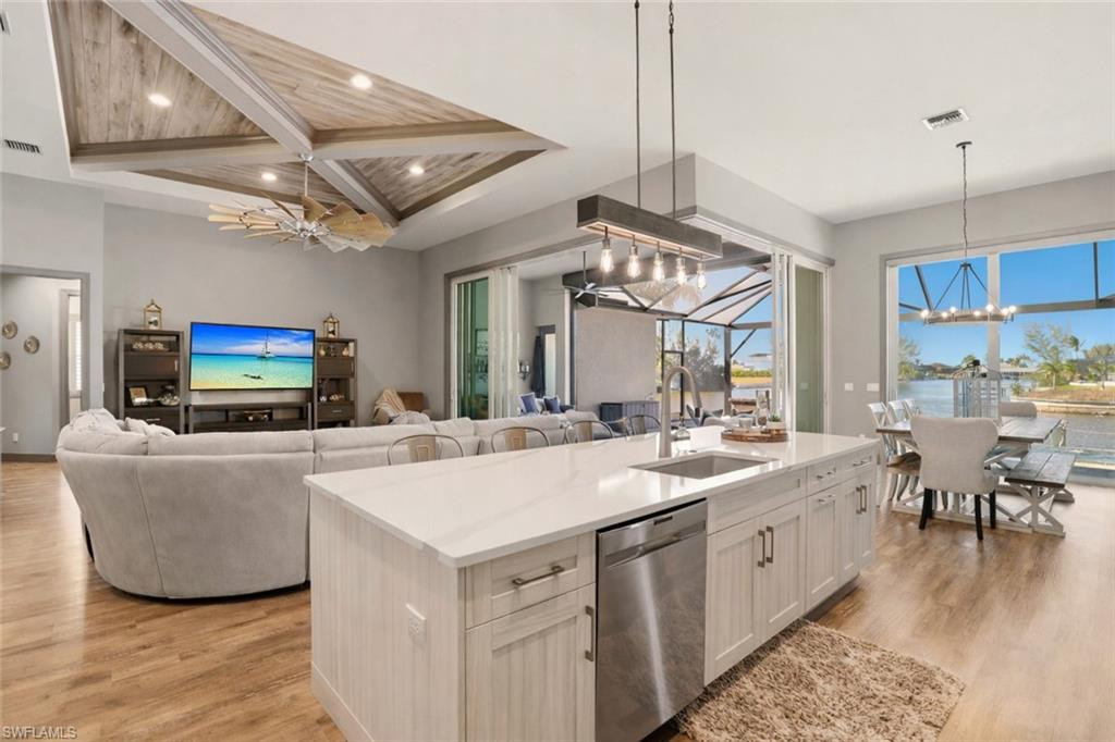 1616 Old Burnt Store Road North Cape Coral, FL 33993 - Photo 13 of 50 From the kitchen, you can watch the family inside and outside. Kitchen featuring a chandelier, stainless steel dishwasher, light stone countertops, open floor plan, and light wood-style flooring.