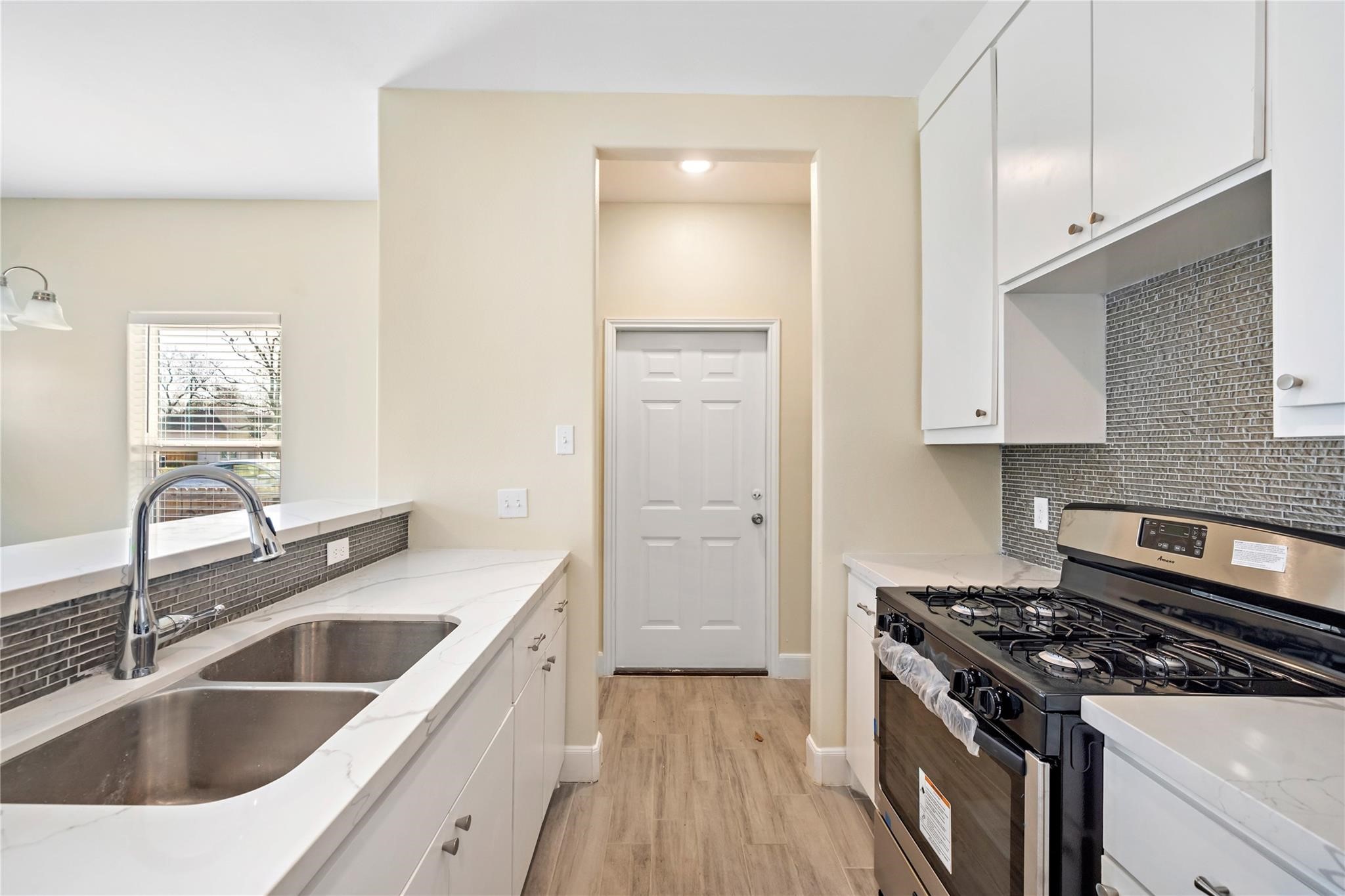 5618 Ridgeway Drive, Unit B Houston, TX 77033 - Photo 6 of 9 This kitchen features sleek stainless steel appliances, a double sink, and modern cabinetry. The light-colored countertops and backsplash complement the neutral walls and wood-style flooring. It offers a bright and functional space with a convenient door leading outside.