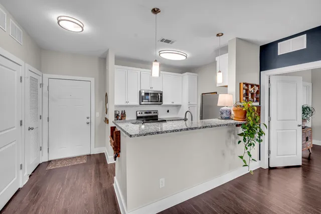 a kitchen with stainless steel appliances granite countertop a refrigerator a sink dishwasher a stove and white cabinets with wooden floor