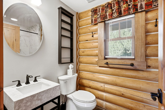 12465 Bone Road Kamas, UT 84036 - Photo 43 of 63 Rustic log cabin bathroom featuring horizontal wood-finish wall paneling, a marble-topped vanity with matte black hardware, an oval framed mirror, a window with wooden surround and horizontal blinds, white subway tile flooring, and vintage-style toilet