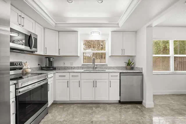 a kitchen with granite countertop white cabinets stainless steel appliances and a window