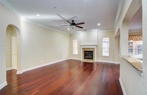 an empty room with wooden floor a ceiling fan a fireplace and windows