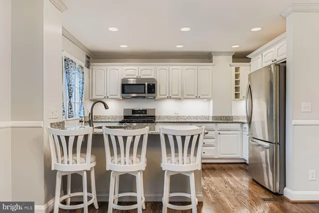 a kitchen with stainless steel appliances granite countertop a stove a sink a refrigerator with white cabinets and wooden floor