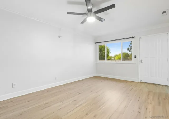 an empty room with wooden floor ceiling fan and windows