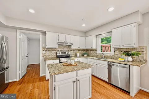 a kitchen with stainless steel appliances granite countertop a stove top oven a sink dishwasher and a refrigerator with wooden floor