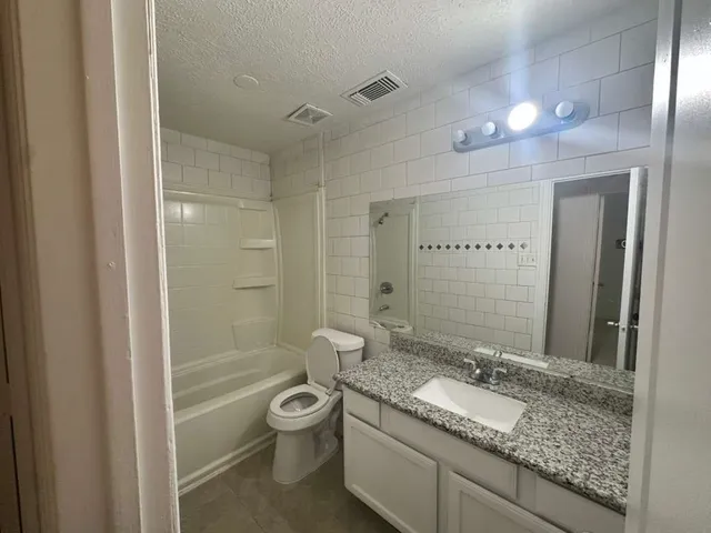a bathroom with a granite countertop sink a toilet a mirror and shower