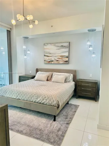 a spacious bedroom with a bed a dresser and chandelier