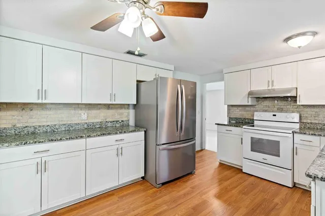 a kitchen with stainless steel appliances granite countertop a refrigerator a stove a sink and white cabinets