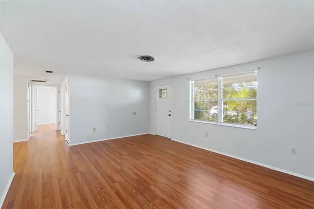 a view of an empty room with wooden floor and a window