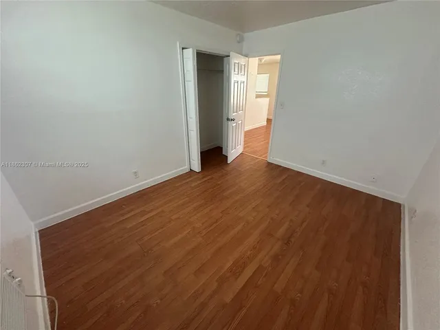 a view of an empty room with wooden floor and closet