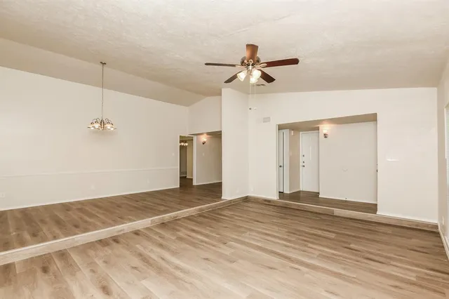 a view of an empty room with wooden floor and a ceiling fan