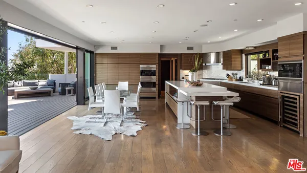 a living room with stainless steel appliances furniture a rug kitchen view and a large window