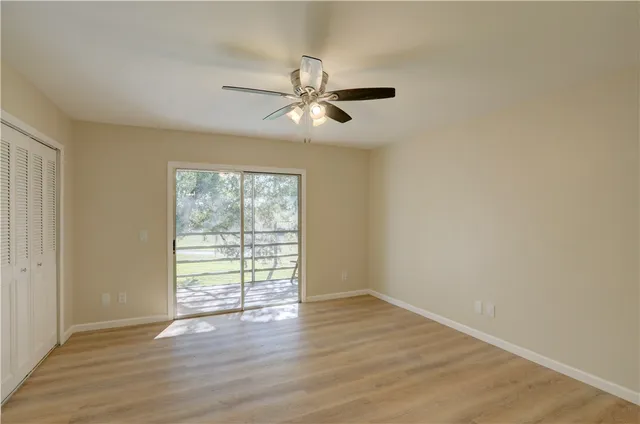 an empty room with wooden floor fan and windows