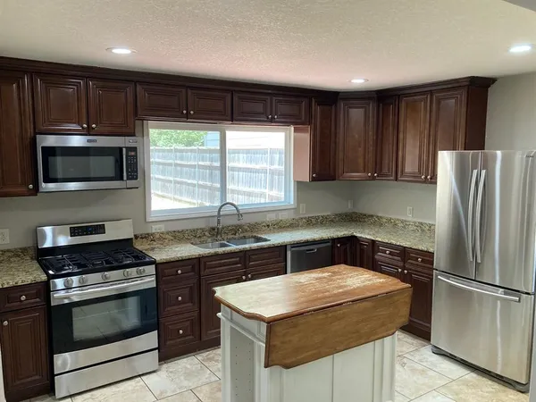 a kitchen with kitchen island granite countertop stainless steel appliances a stove cabinets and a window