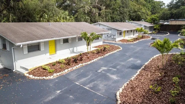 a view of a white house with a yard plants and large tree
