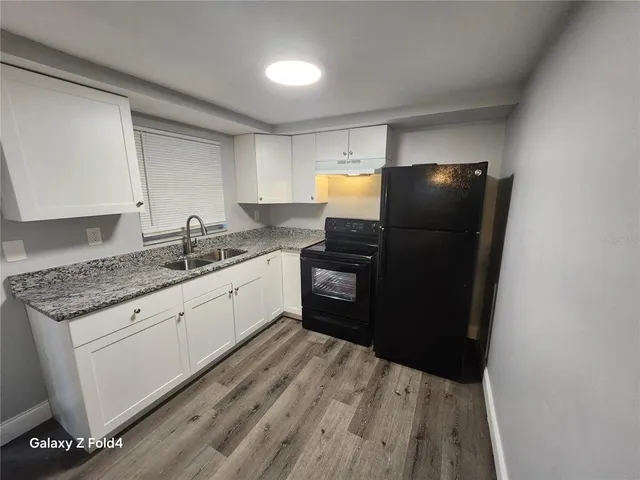 a kitchen with granite countertop a refrigerator a sink and white cabinets