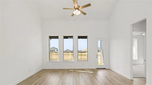 an empty room with wooden floor fan and windows