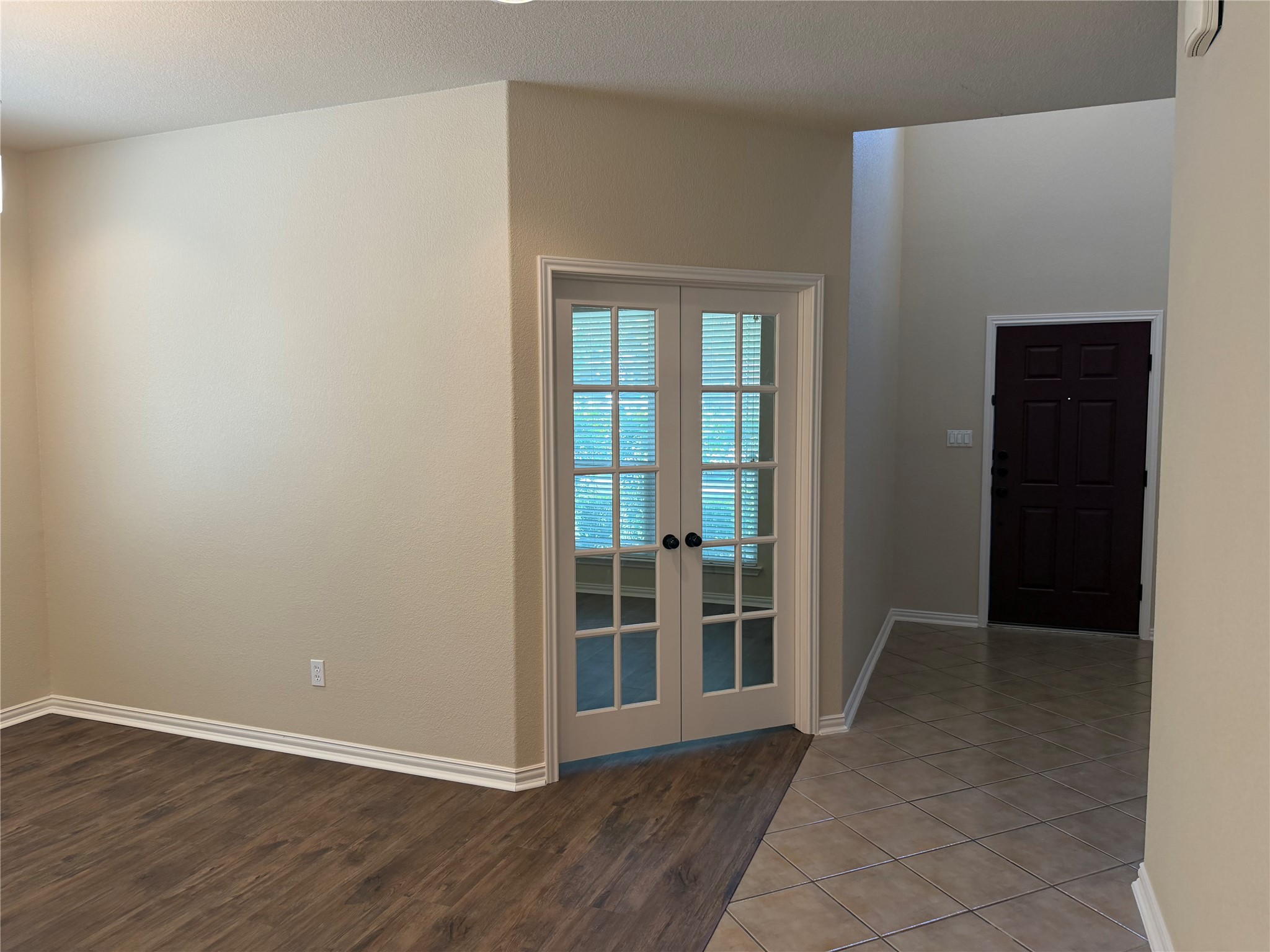 3021 Grand Mission Way Pflugerville, TX 78660 - Photo 6 of 31 French doors open into a versatile living space, contrasting with the entryway's tiled floor and dark front door.
