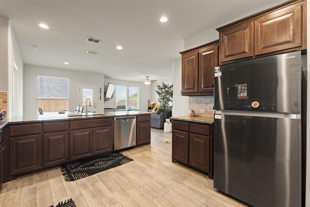 1812 Millbrae Road Cleburne, TX 76033 - Photo 6 of 30 Kitchen featuring wood-finish flooring, dark wood cabinetry, light-toned countertops, a stainless steel dishwasher, and a stainless steel refrigerator
