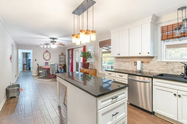 a kitchen with granite countertop a sink dishwasher a stove and a dining table with wooden floor