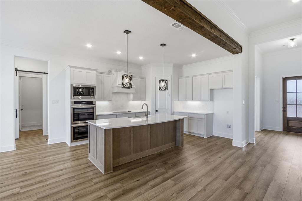 810 Vly Rdg Road Van Alstyne, TX 75495 - Photo 5 of 39 Dual tone kitchen featuring dual tone cabinets, an island with sink, pendant lighting, ornamental molding, and light wood finished floors