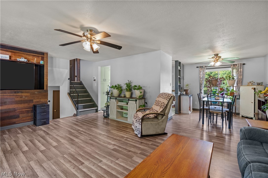 13548 Holland Road Brook Park, OH 44142 - Photo 6 of 27 Spacious open-concept interior featuring wood-finish flooring, a wood accent wall with built-in shelving, two ceiling fans with integrated lighting, and a staircase with a metal handrail