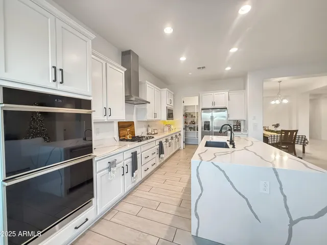 a large kitchen with stainless steel appliances kitchen island granite countertop a refrigerator a stove a sink and white cabinets with wooden floor