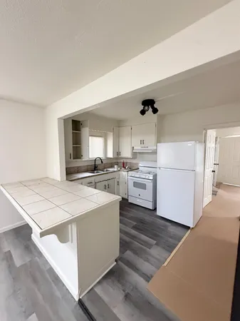 a open kitchen with kitchen island a stove a sink dishwasher and white cabinets with wooden floor