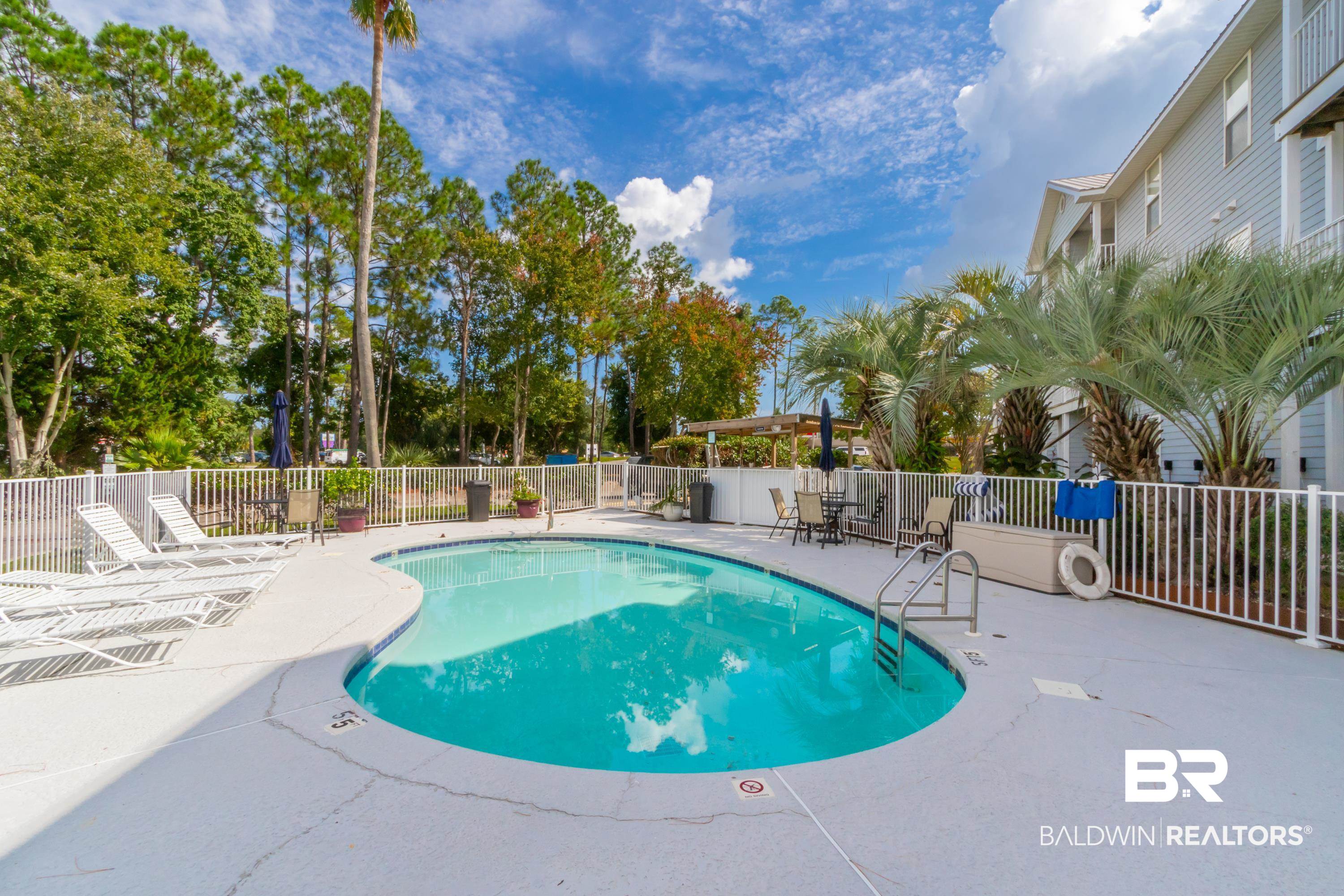 25957 Canal Road, Unit 208 Orange Beach, AL 36561 - Photo 25 of 28 Fenced swimming pool area featuring a free-form pool, surrounding concrete deck, and mature trees