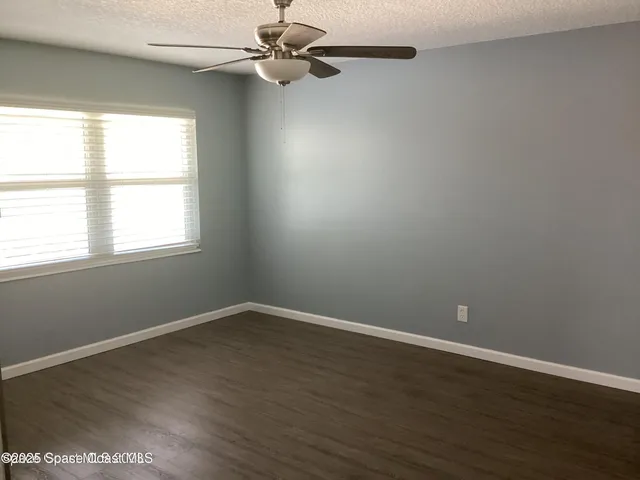 an empty room with wooden floor fan and windows
