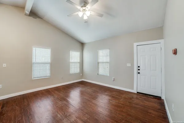 an empty room with wooden floor chandelier fan and windows