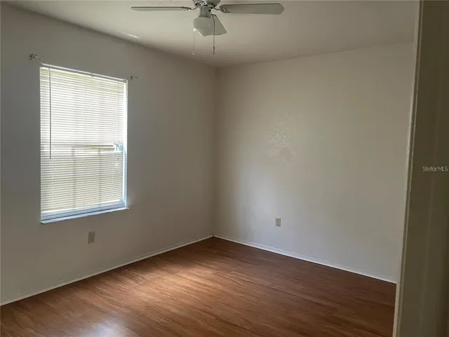 an empty room with wooden floor chandelier fan and windows
