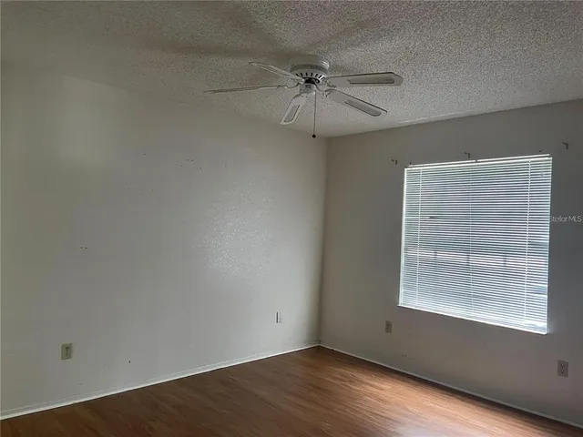 an empty room with wooden floor fan and windows