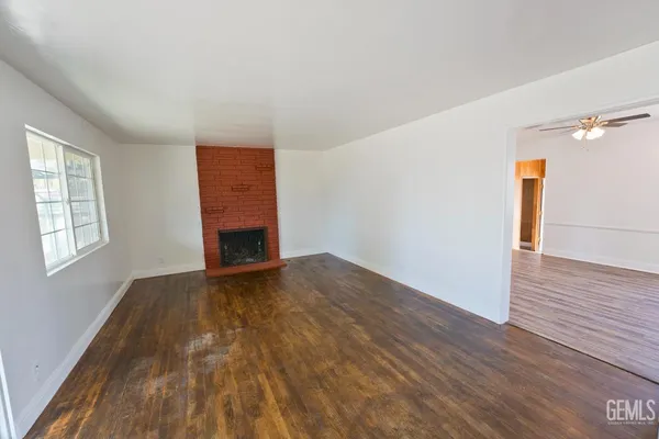 a view of an empty room with wooden floor fireplace and a window