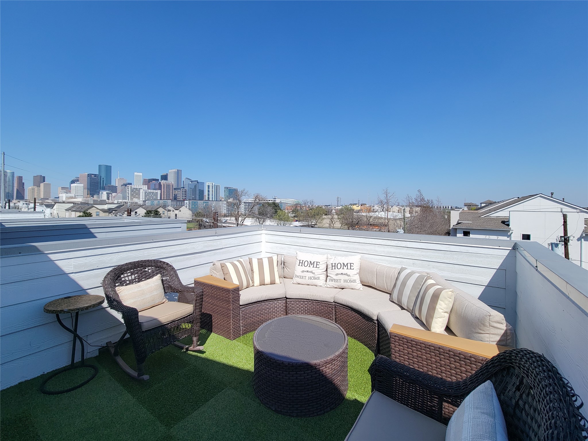 Welcome to Eado Living! This rooftop patio offers a cozy seating area with wicker furniture and a stunning city skyline view, perfect for relaxation and entertaining.