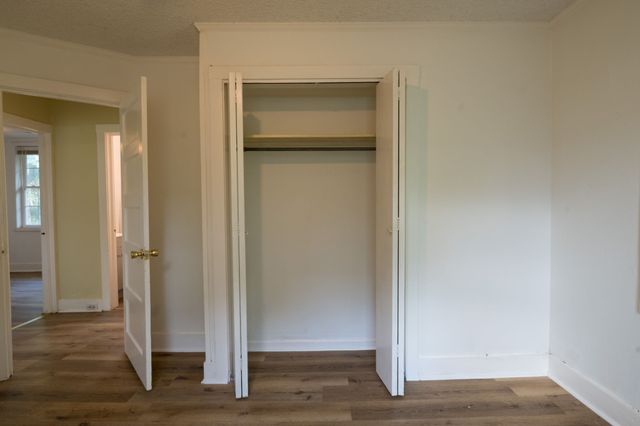 an empty room with wooden floor closet and windows